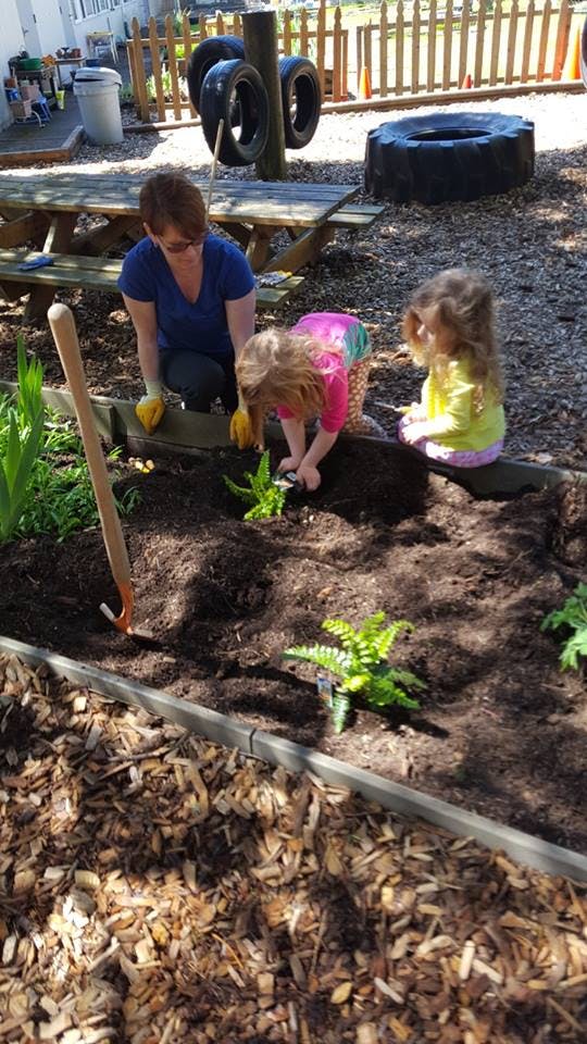 Person and two children planting in a garden bed