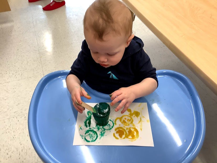 Child in a high chair painting with green and yellow paint