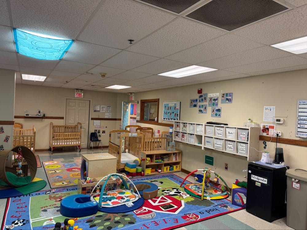 Baby room with multiple cribs, colorful playmats, and storage shelves