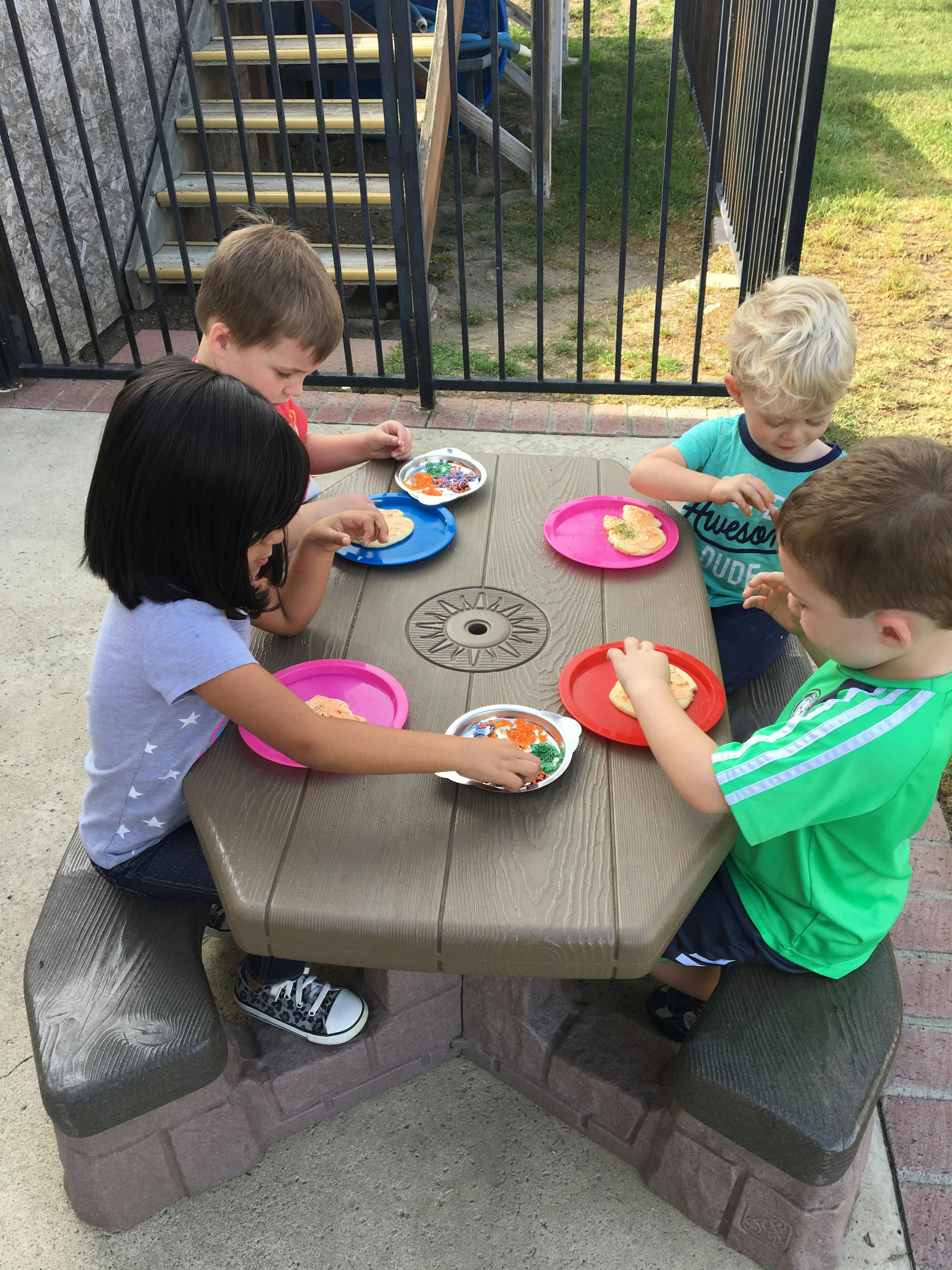 Four children sitting at a picnic table with plates of food