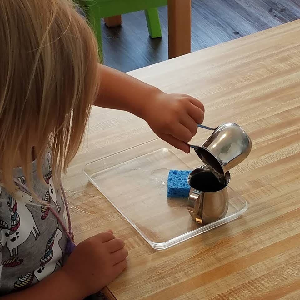 Child pouring liquid from one metal pitcher into another