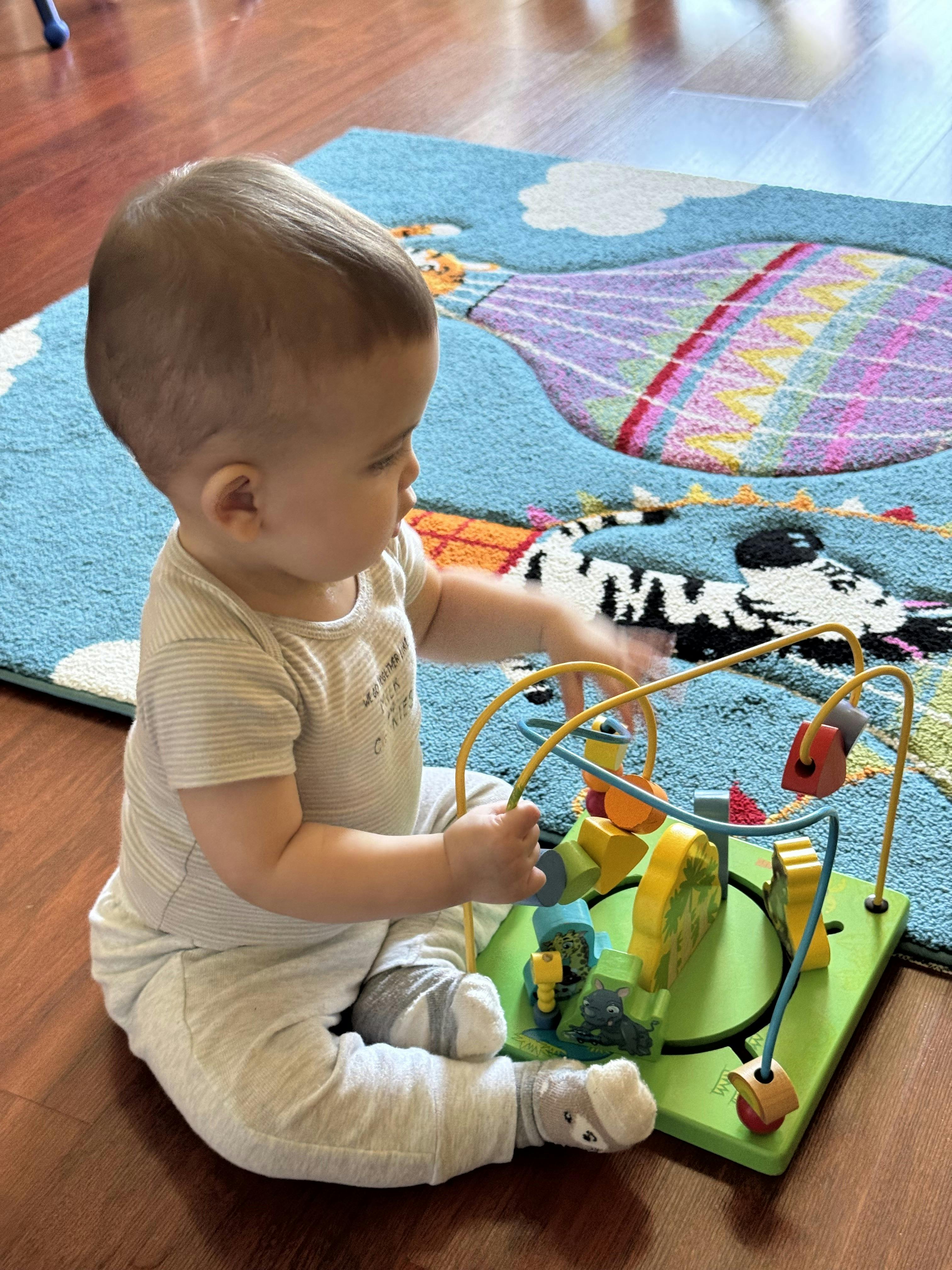 Child sitting on a wooden floor playing with a bead maze toy