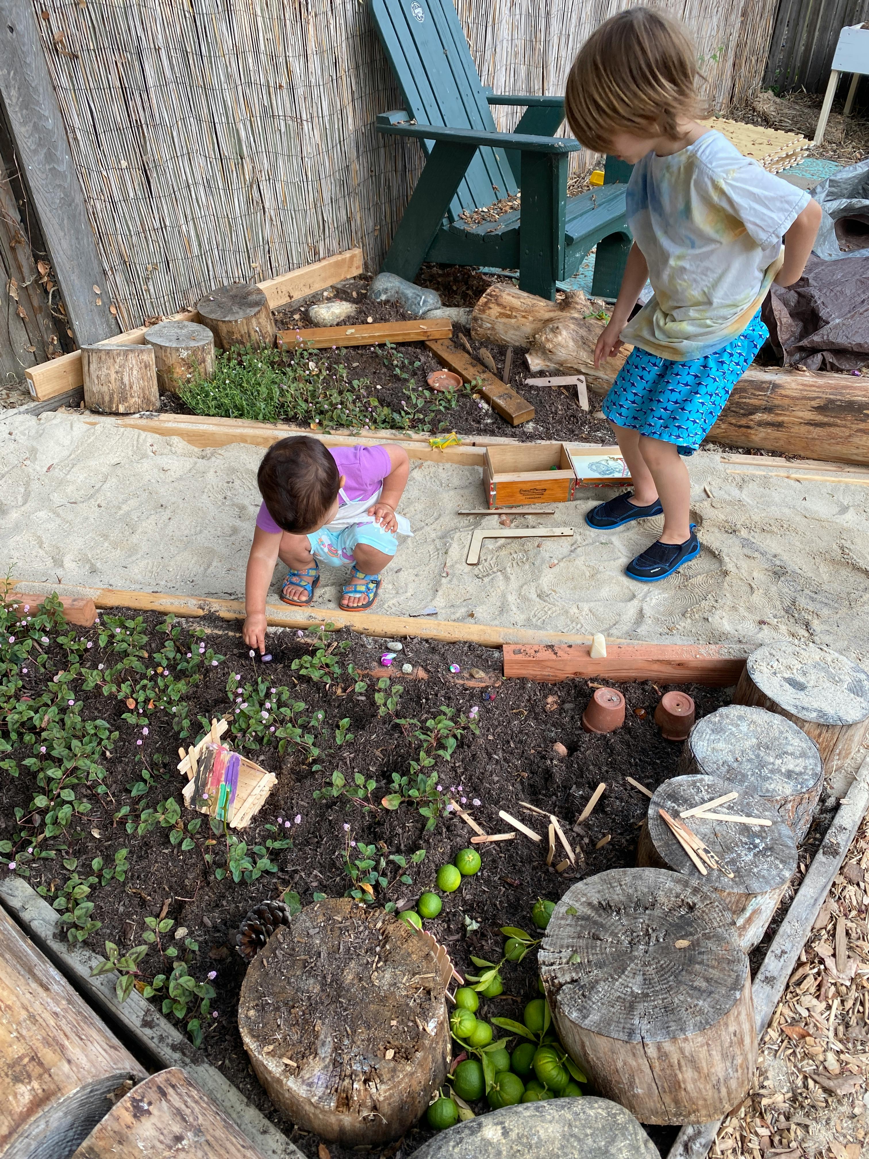 Two children playing in a garden with sand and plants