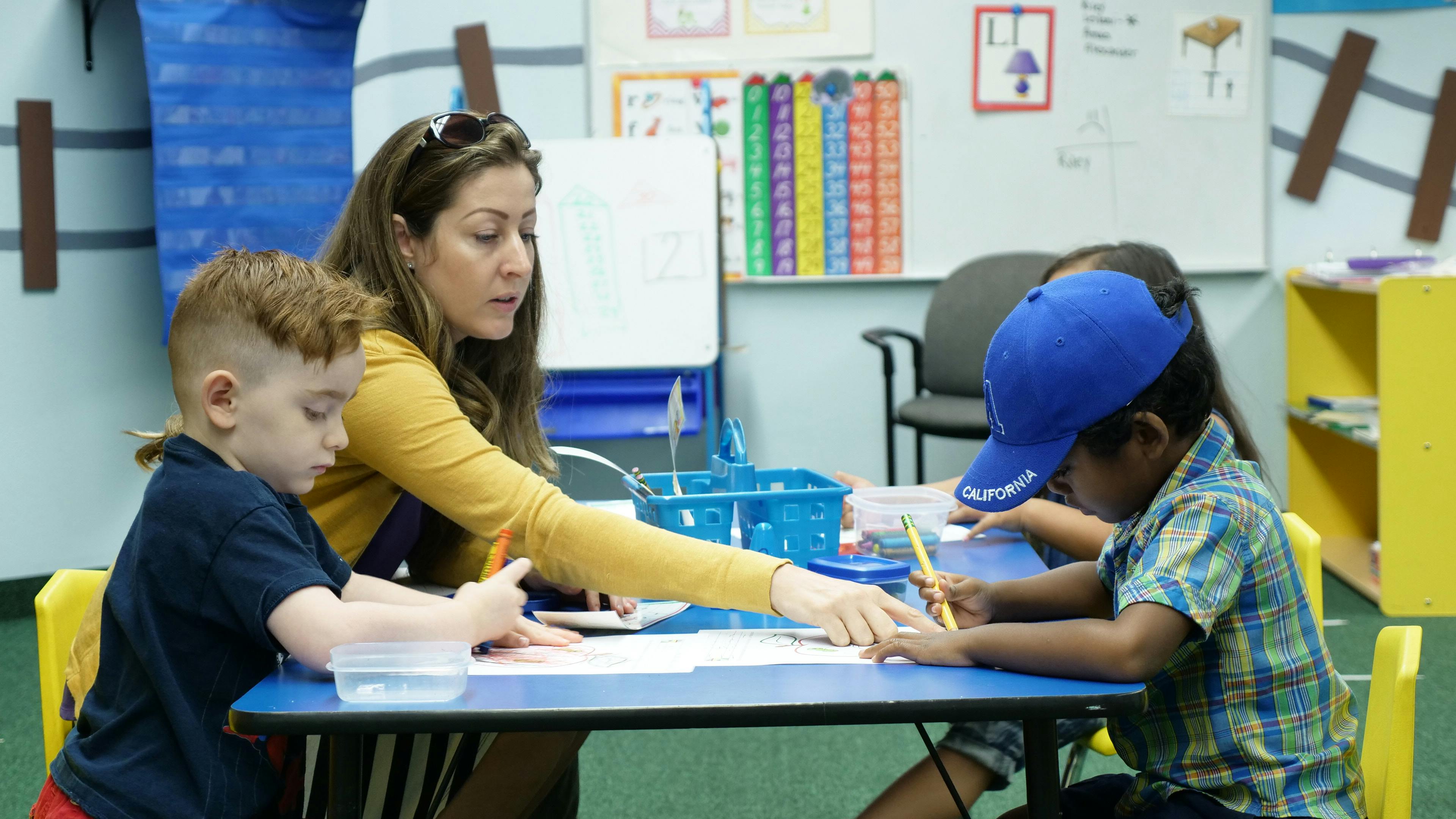 Adult and two children drawing at a table in a classroom