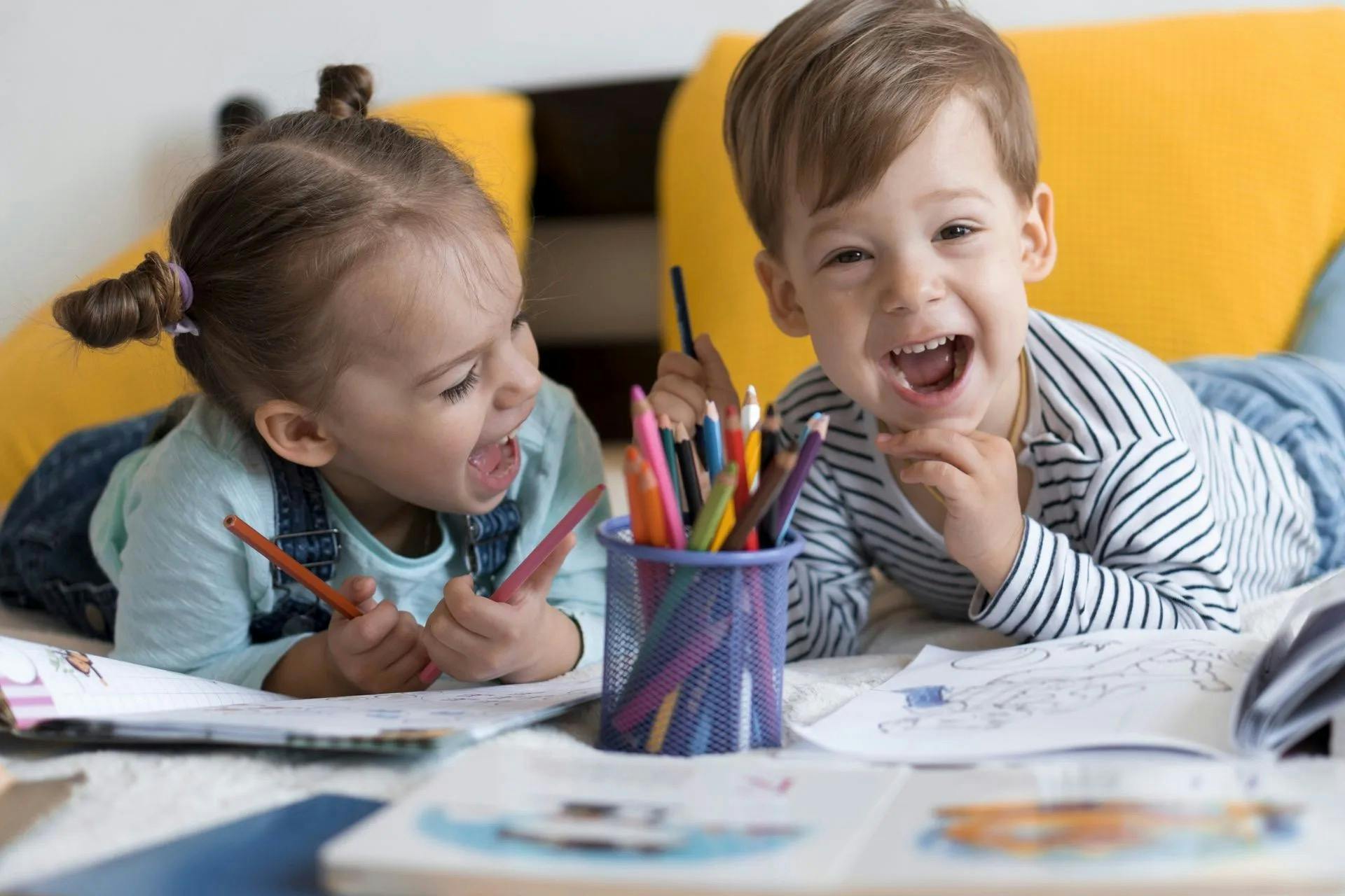 Two children coloring together with pencils on a bed