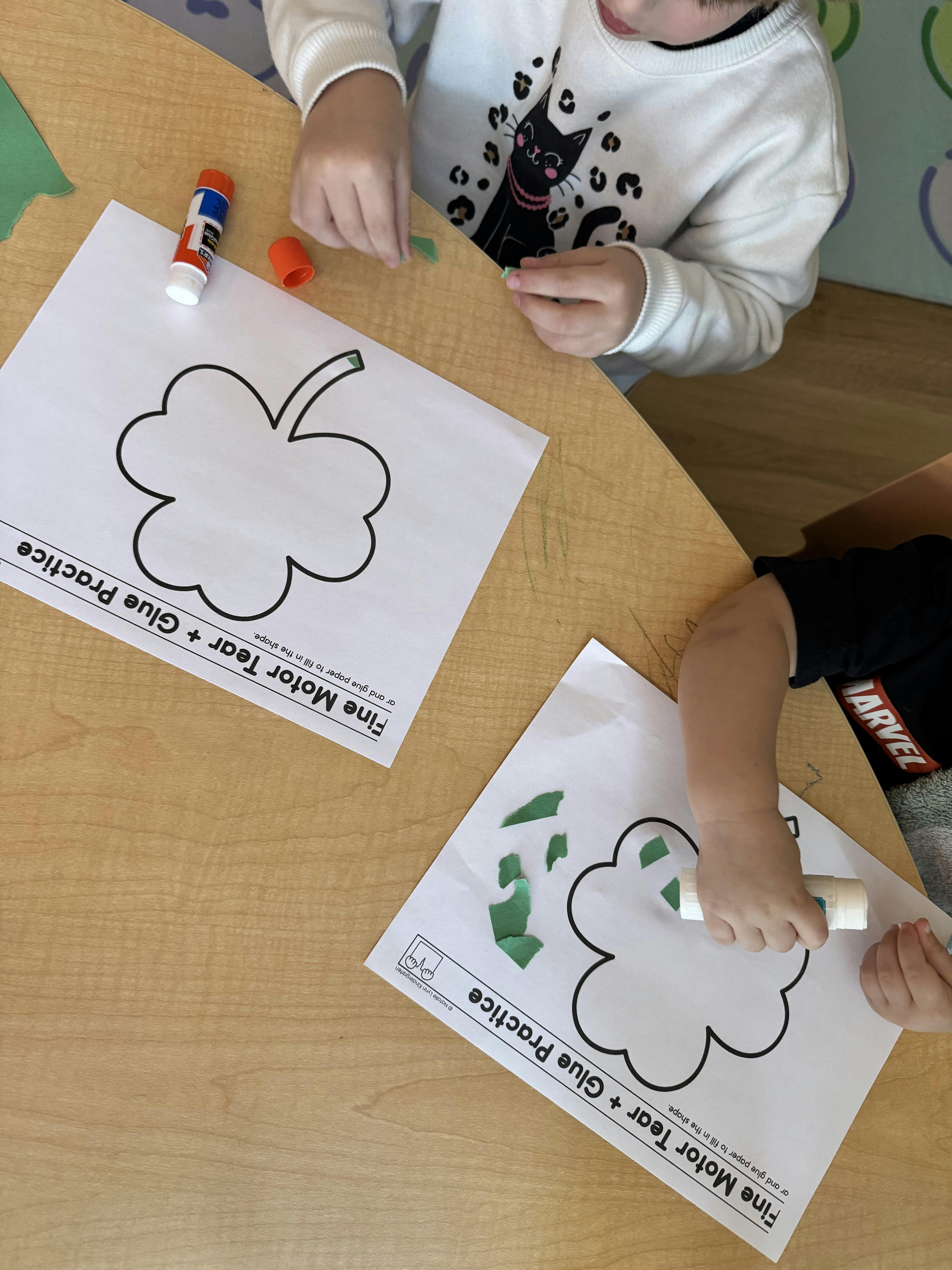 Children doing a 'Fine Motor Tear + Glue Practice' activity with shamrock shapes