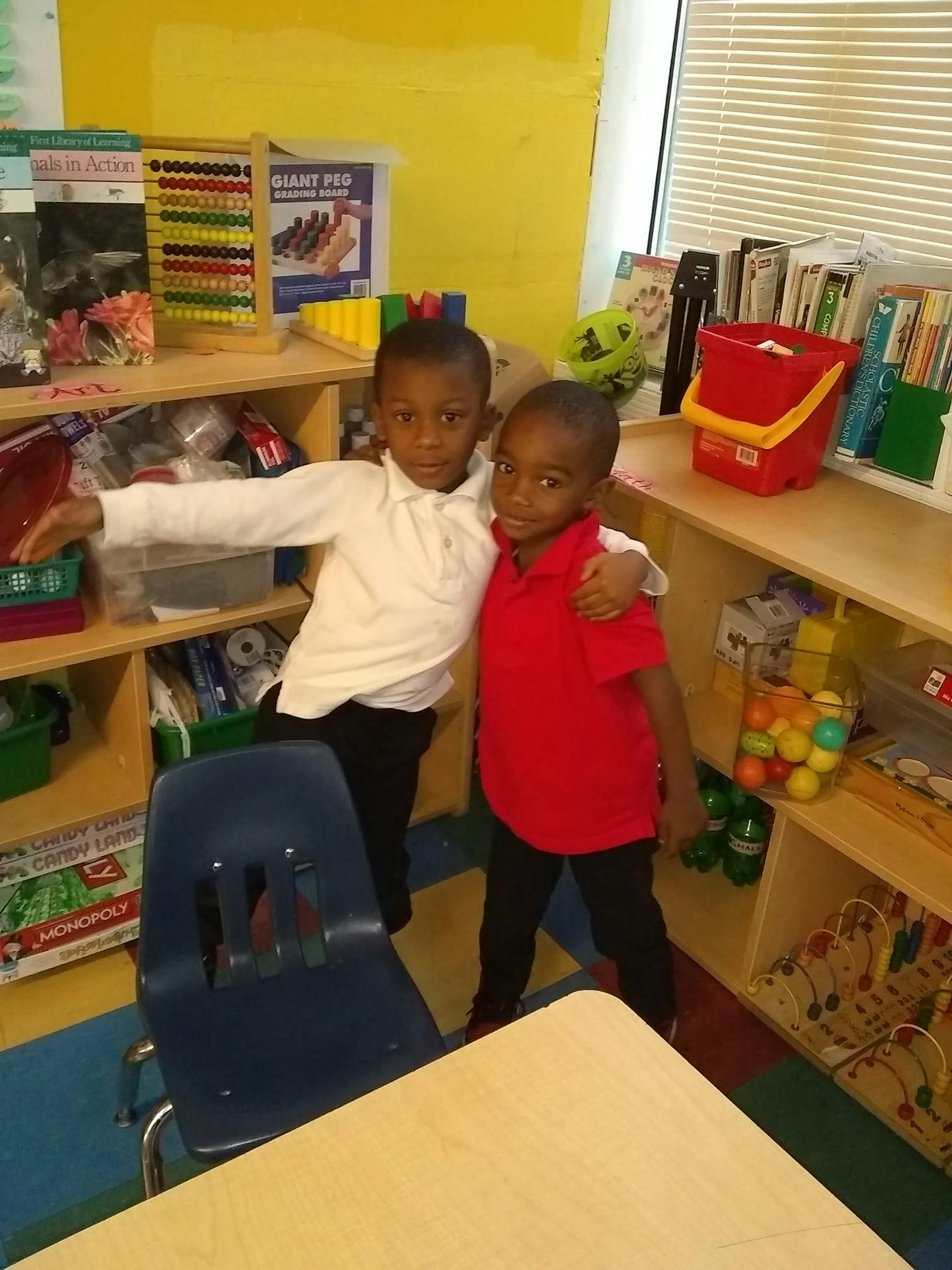 Two children standing in a classroom, one with arm around the other