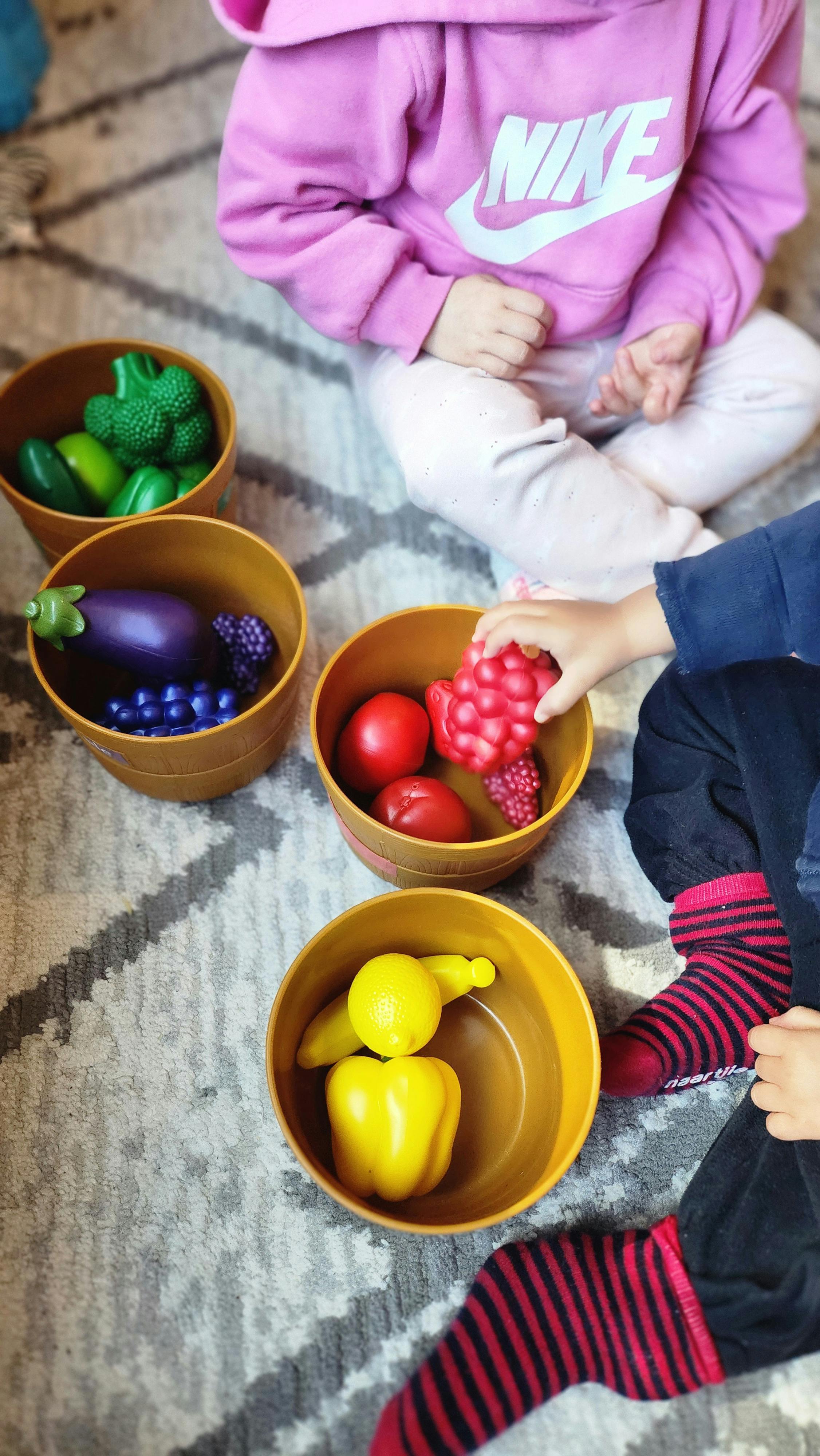 Children playing with toy fruits and vegetables in bowls