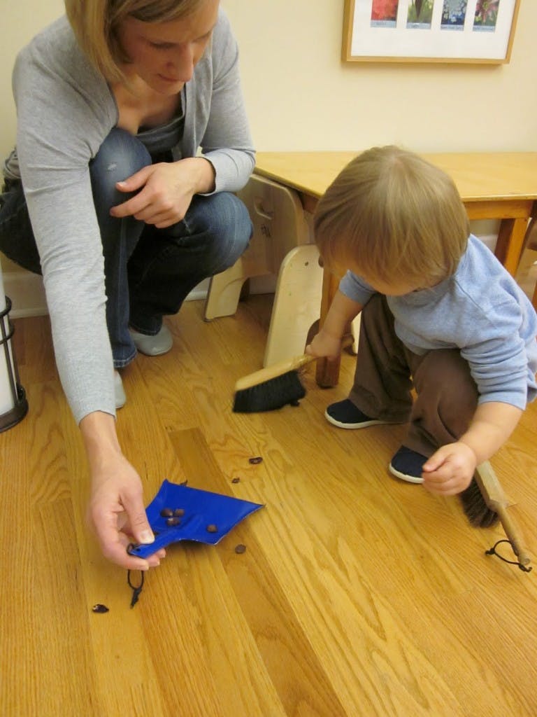 Person and child sweeping small objects into a dustpan on a wooden floor