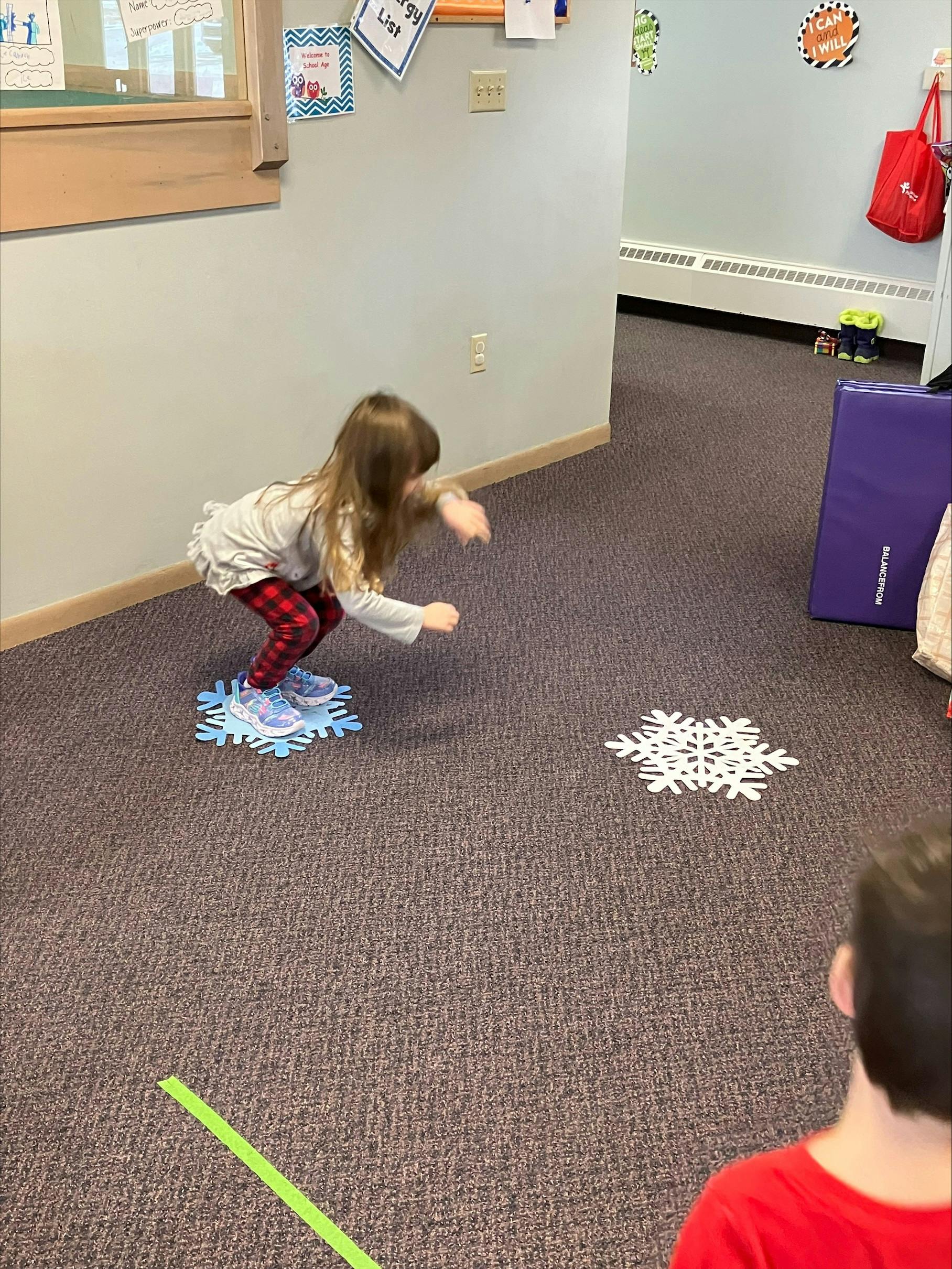 Child crouching on a blue snowflake cutout on a carpeted floor