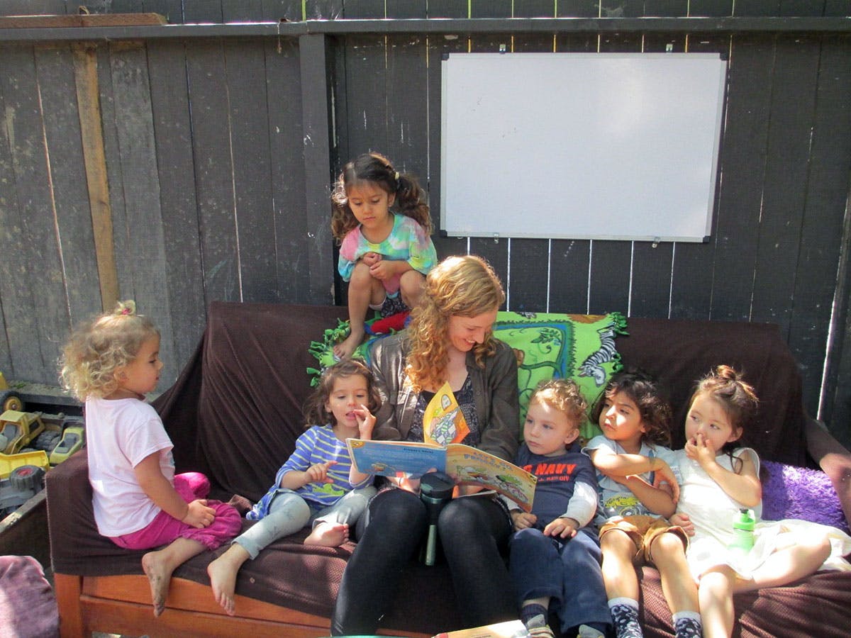 Adult reading a book to multiple children on a couch