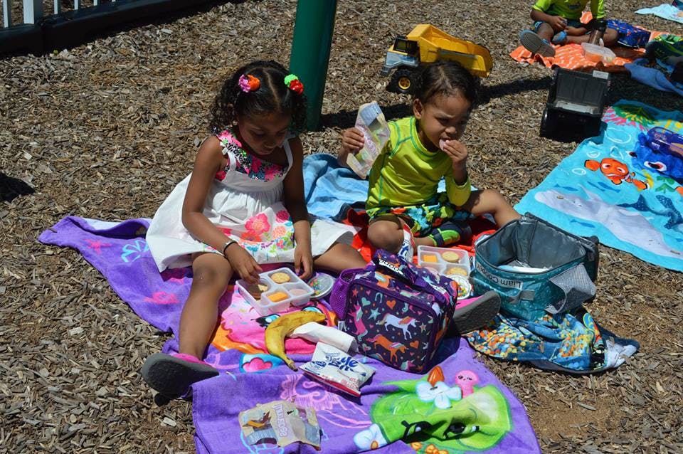 Two children sitting on blankets outdoors, eating snacks