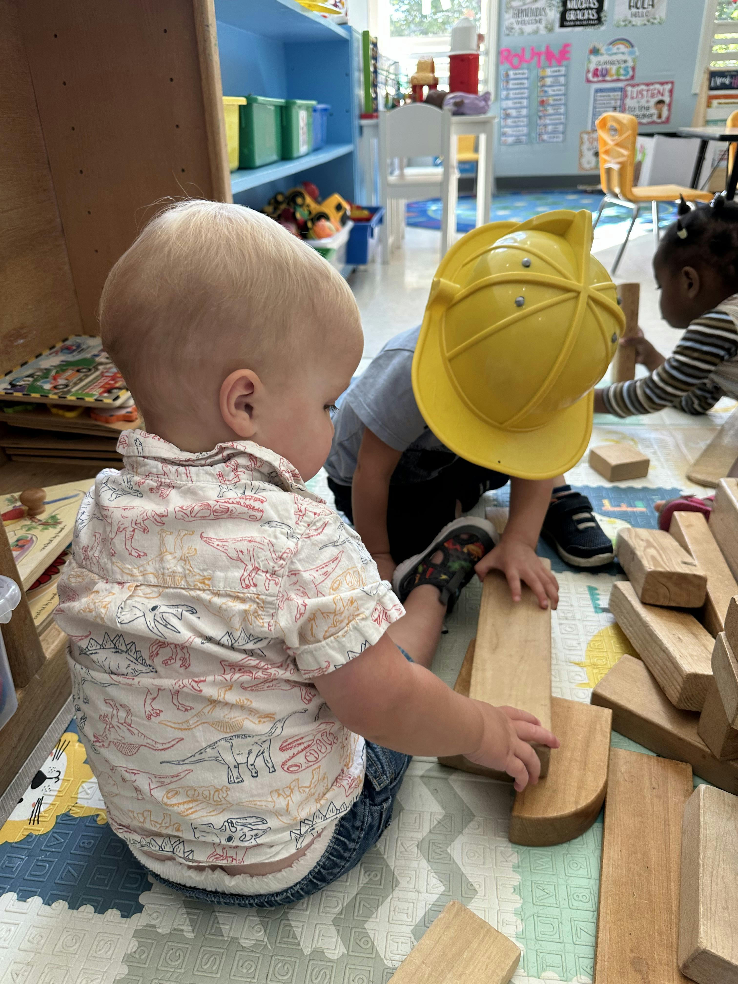 Three children playing with wooden blocks on a mat in a classroom