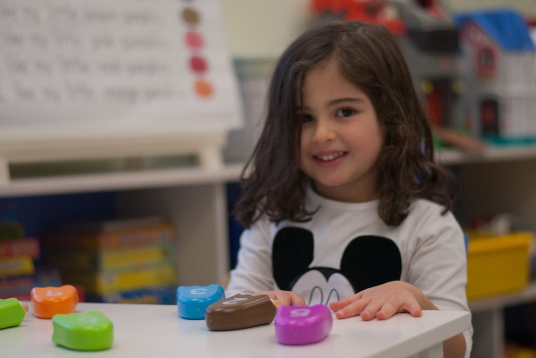 Child in a Mickey Mouse shirt sitting at a table with colorful toys