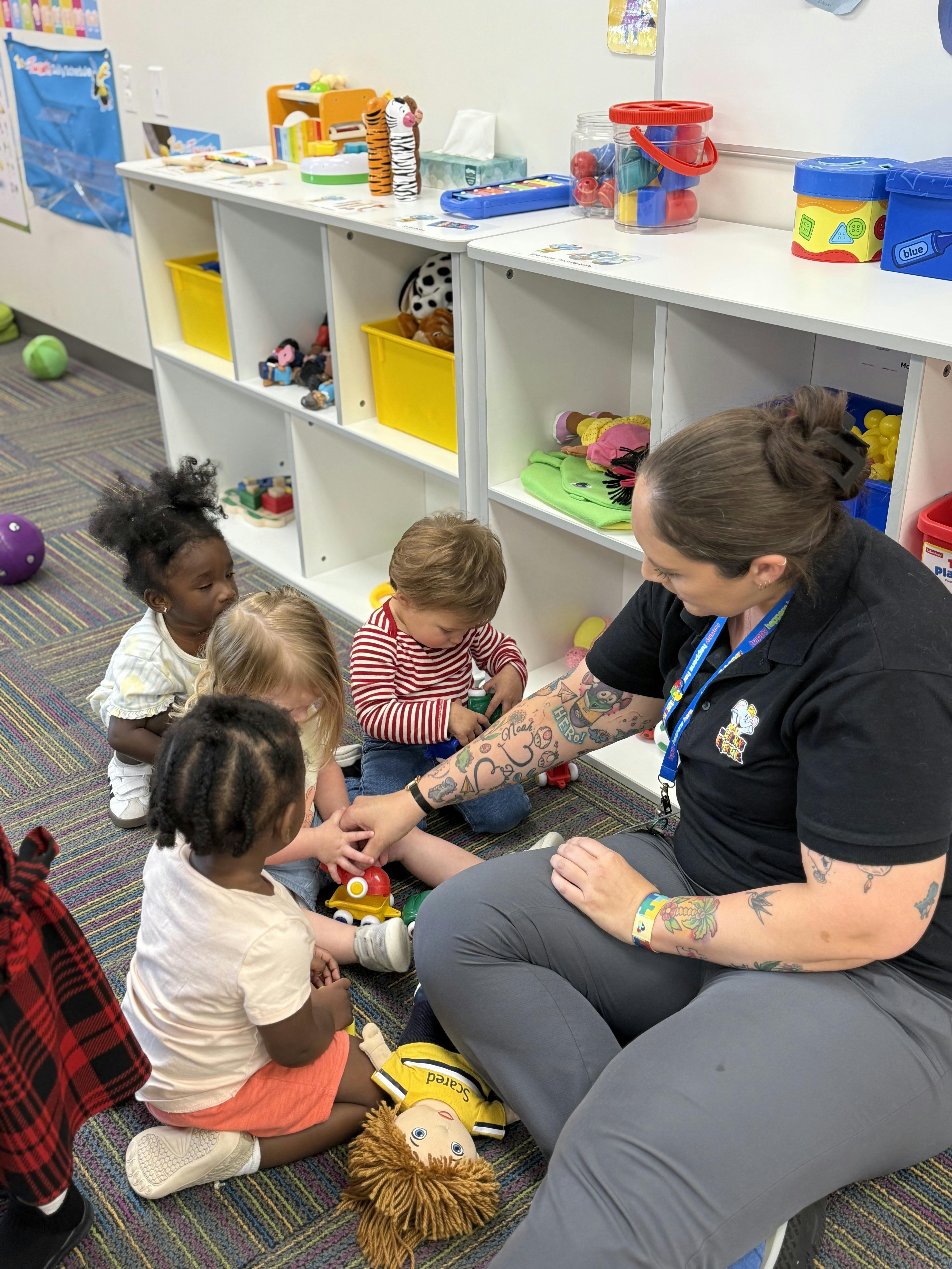 Adult and three children sitting on floor playing with toys in a classroom