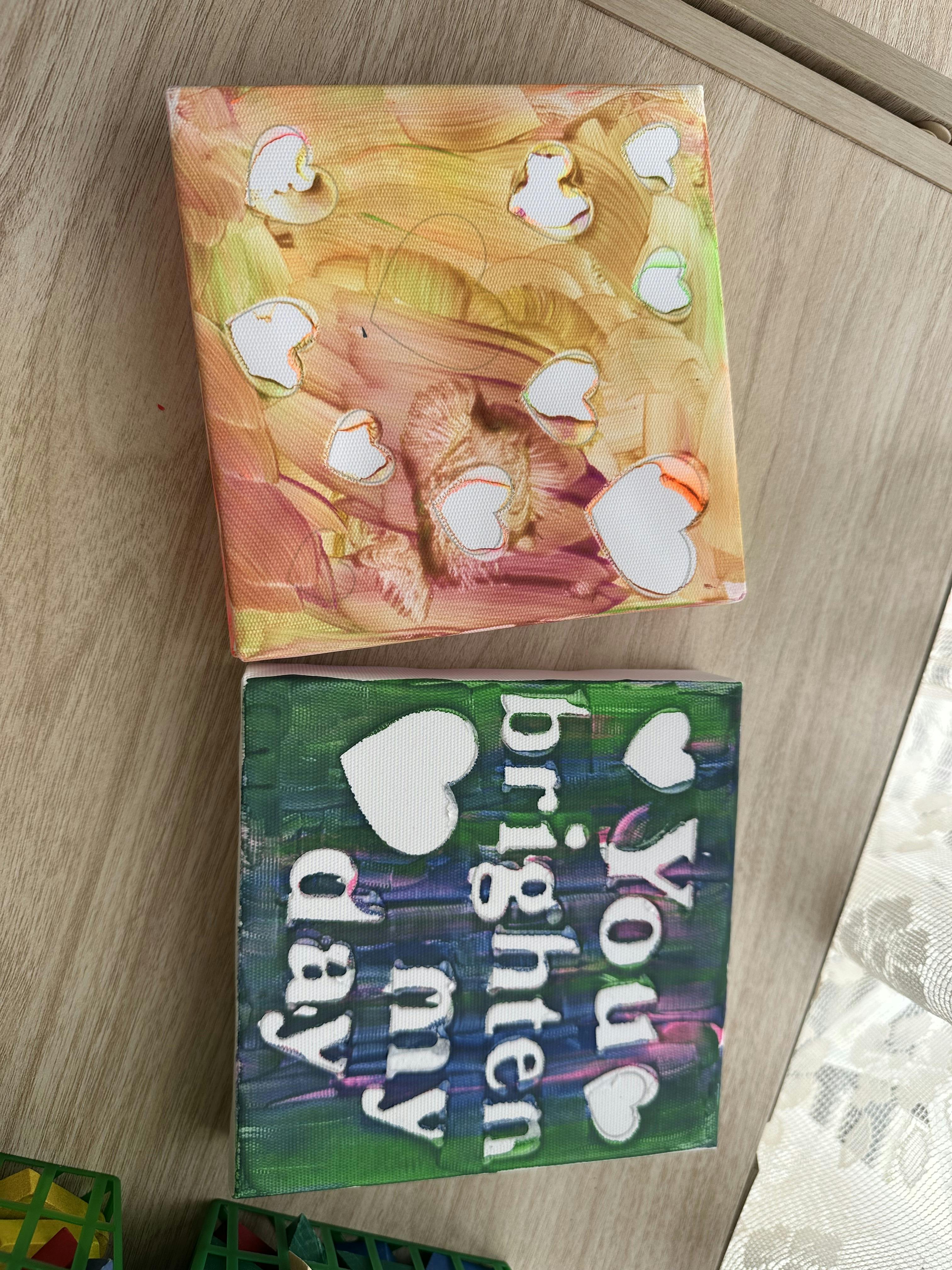 two canvases, one with hearts and paint, one with hearts and text reading "You brighten my day"