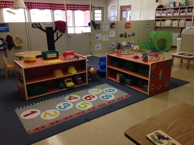 Classroom with shelves of toys, a number rug, and child-sized furniture