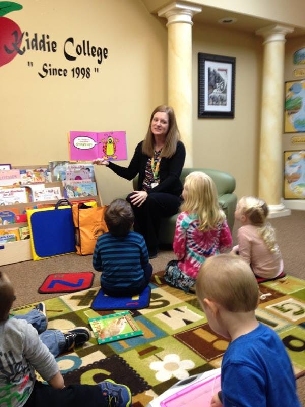 Person reading a book to a group of children sitting on the floor