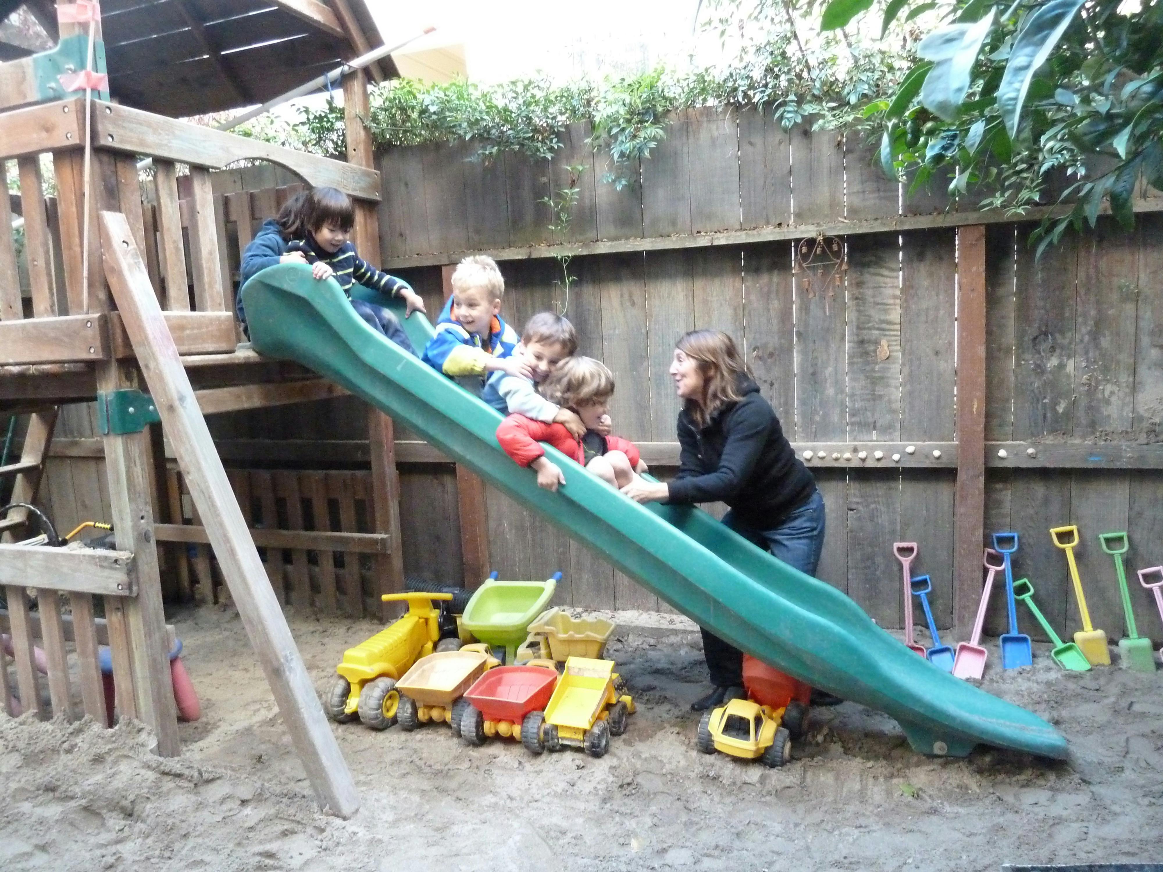 Adult helping children on a playground slide