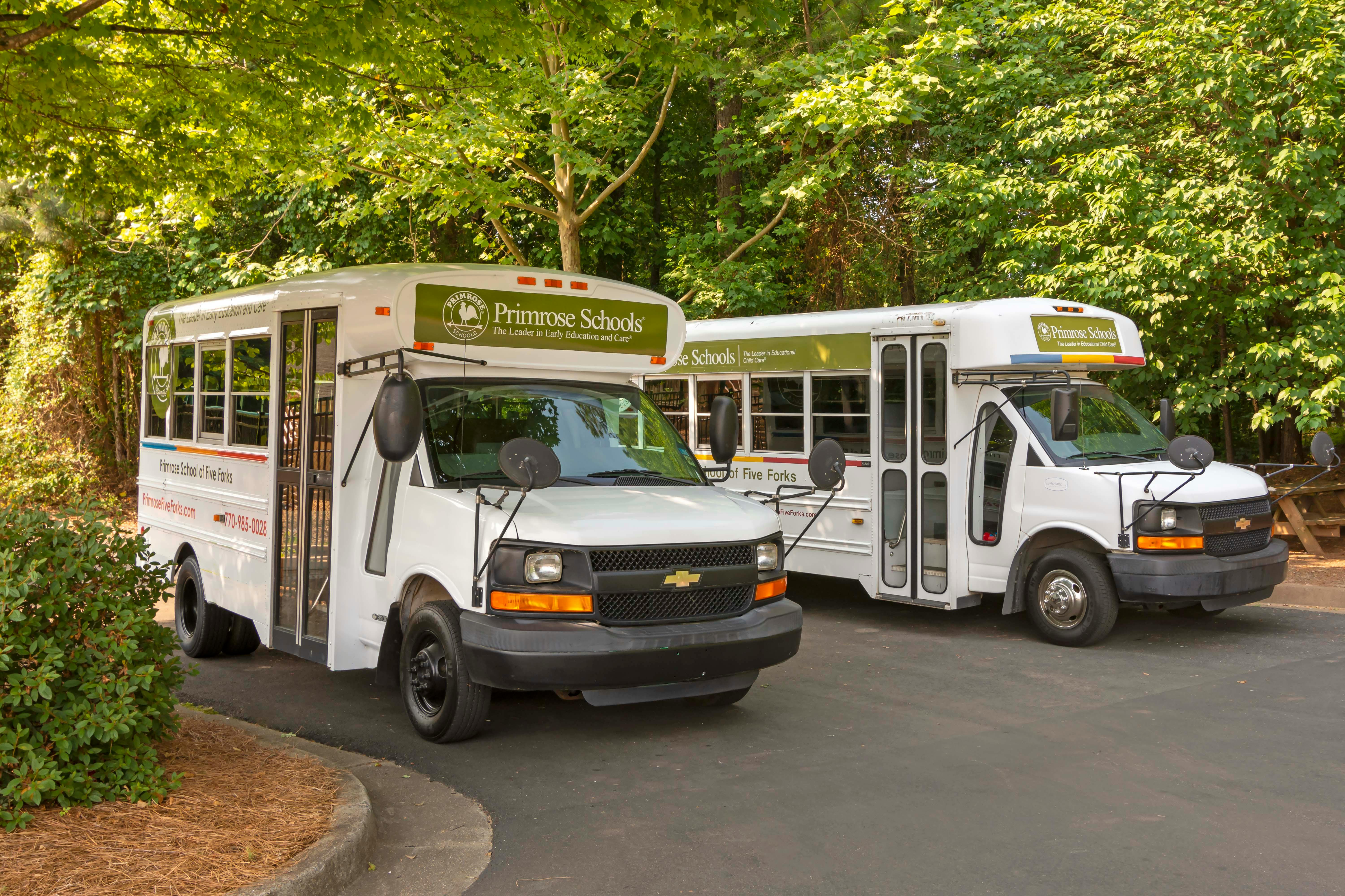 Two white Primrose Schools shuttle buses parked on an asphalt lot