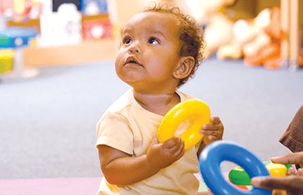 Child holding a yellow ring toy and looking up