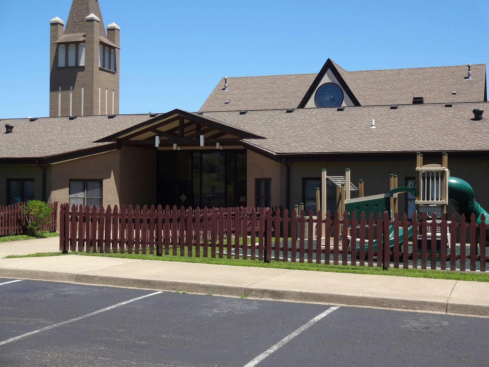 Building with a steeple and a playground behind a fence
