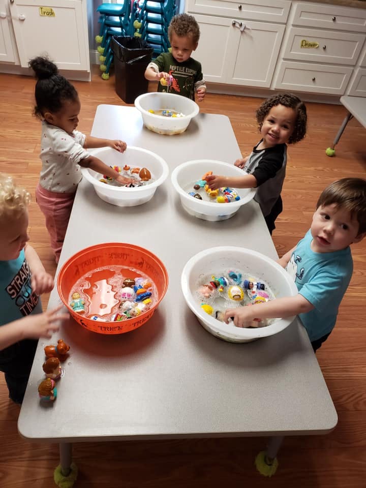 Children playing with toys in bowls of water at a table