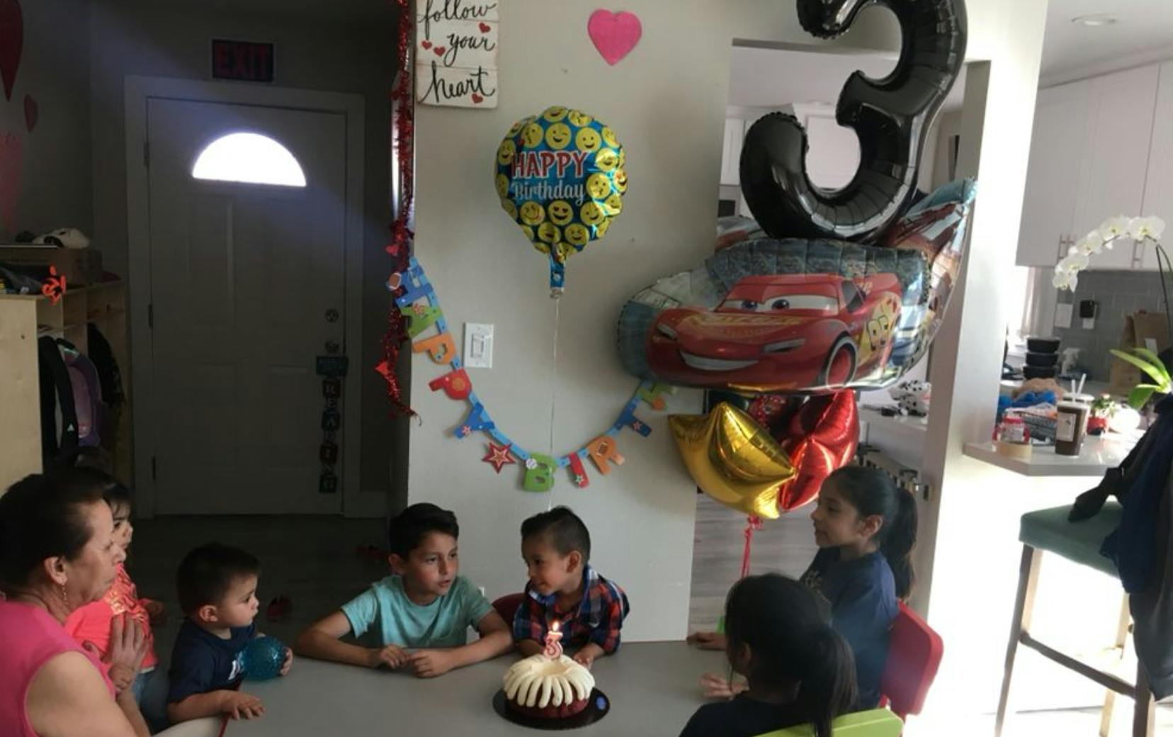 People and children gathered around a birthday cake with balloons