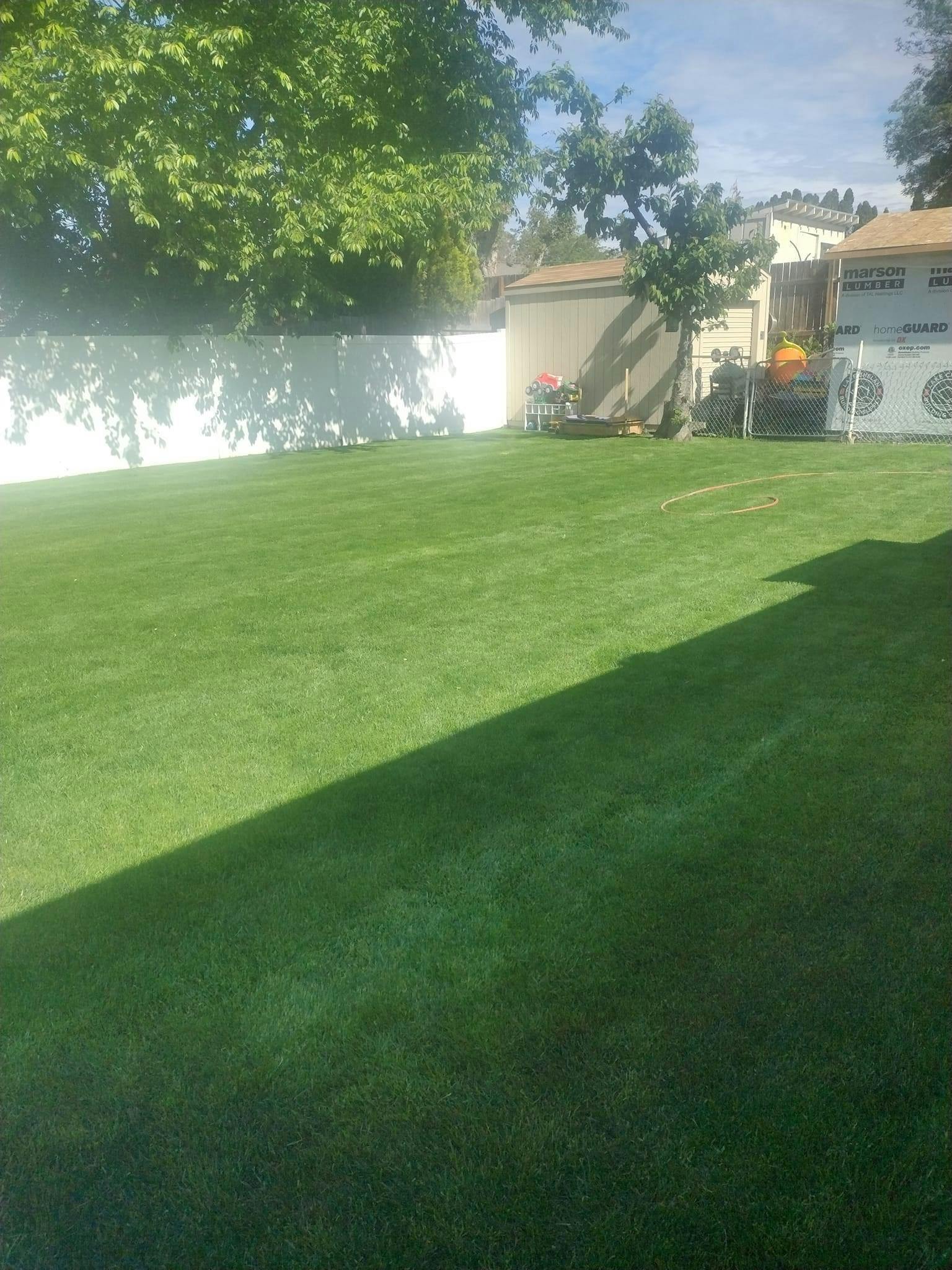 Green lawn with a white fence and trees in the background
