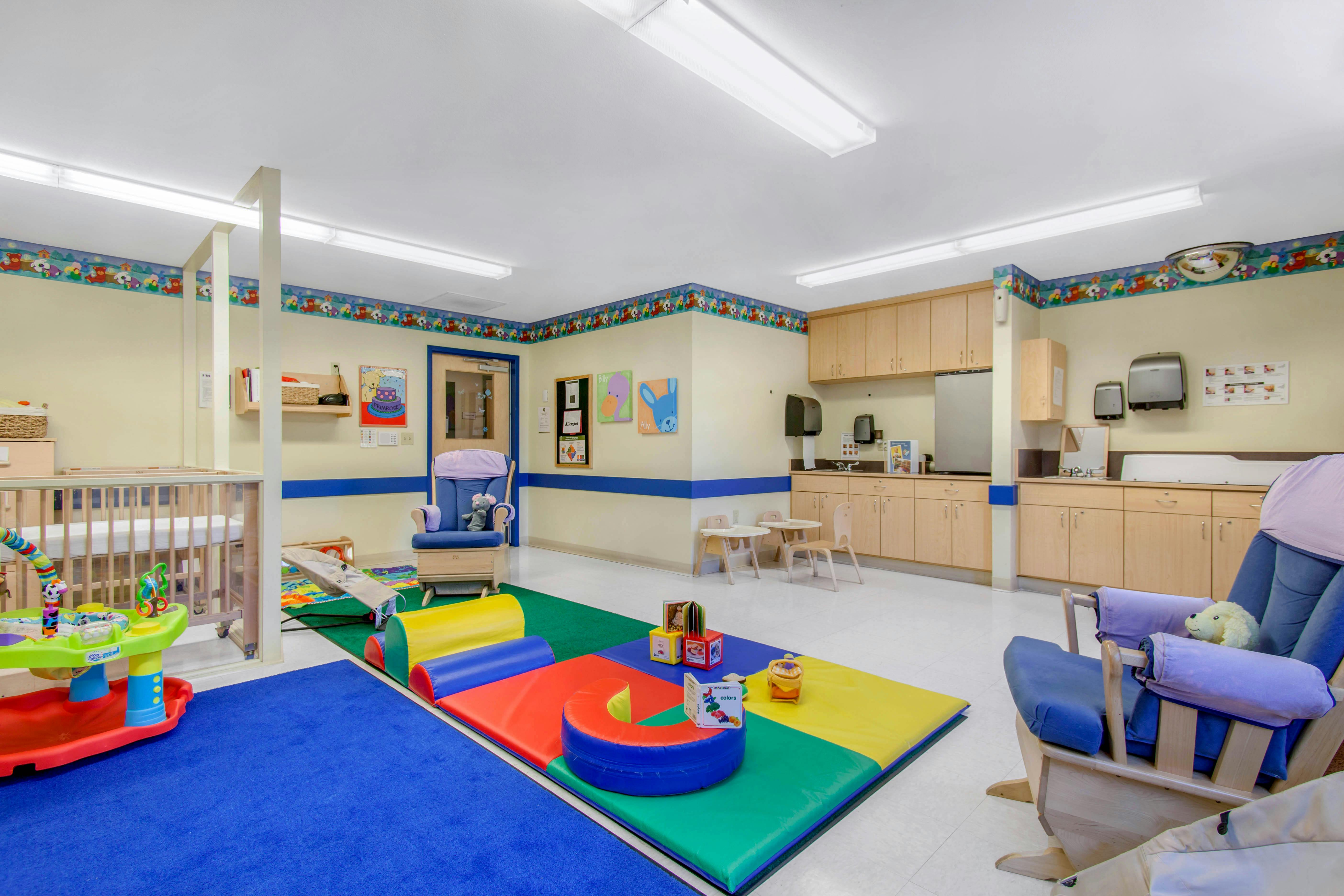 A colorful childcare room with play mats, a crib, and a changing station