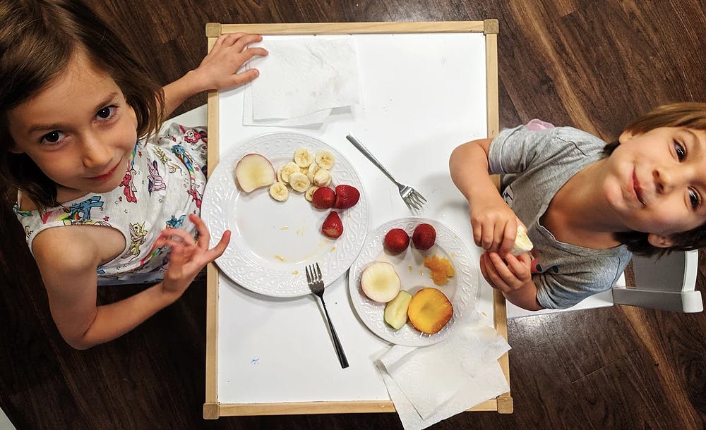 Two children at a table with plates of fruit
