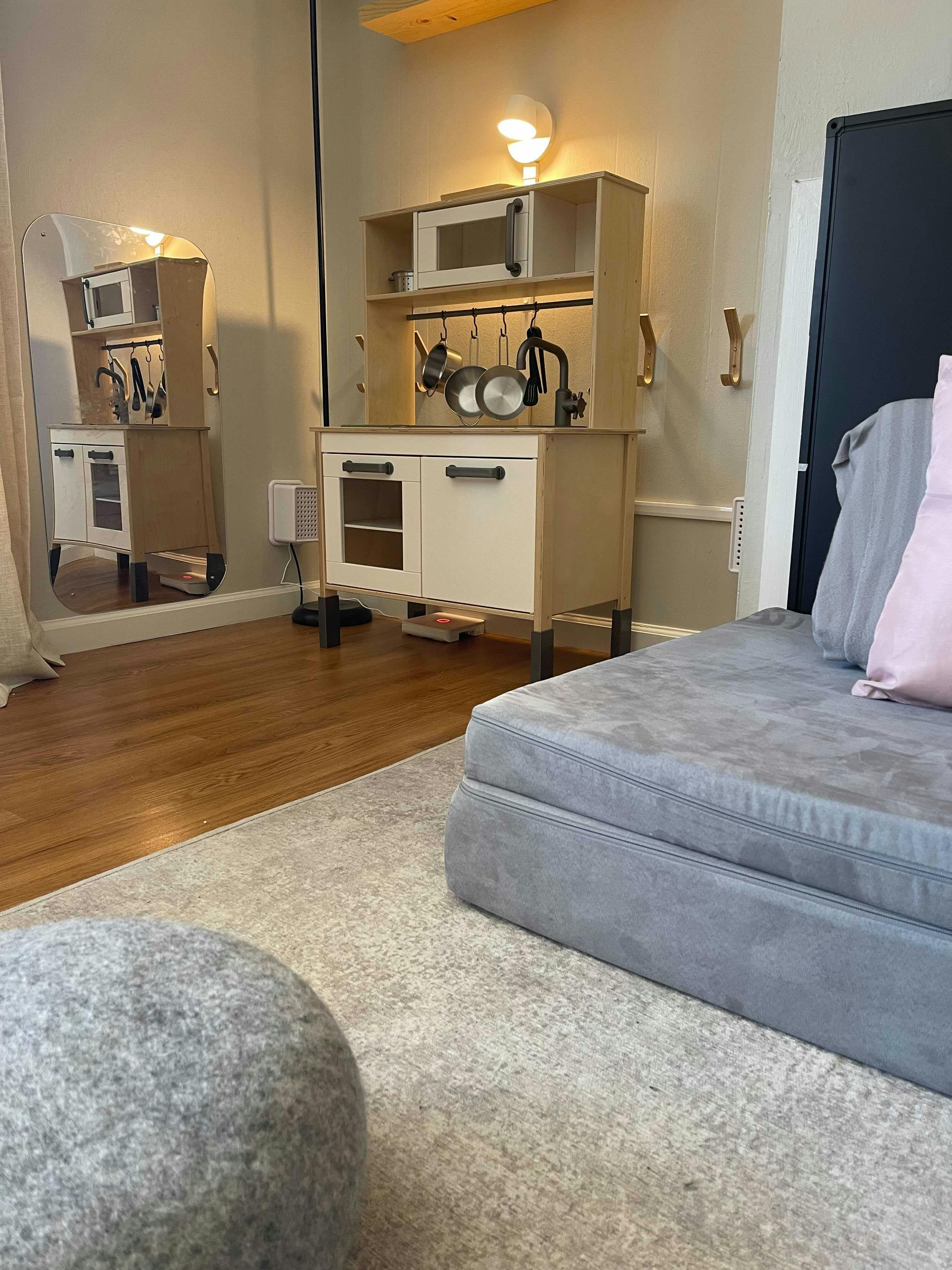 Toy kitchen set with pots and pans, next to a gray sofa