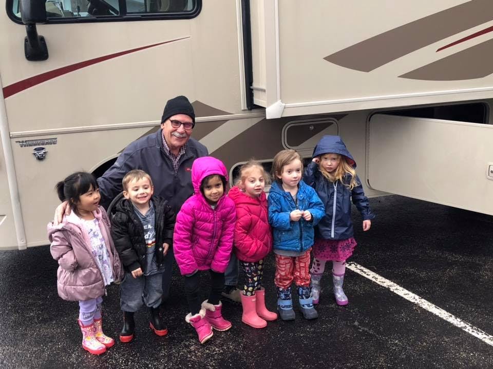 Adult and multiple children standing in front of a large vehicle