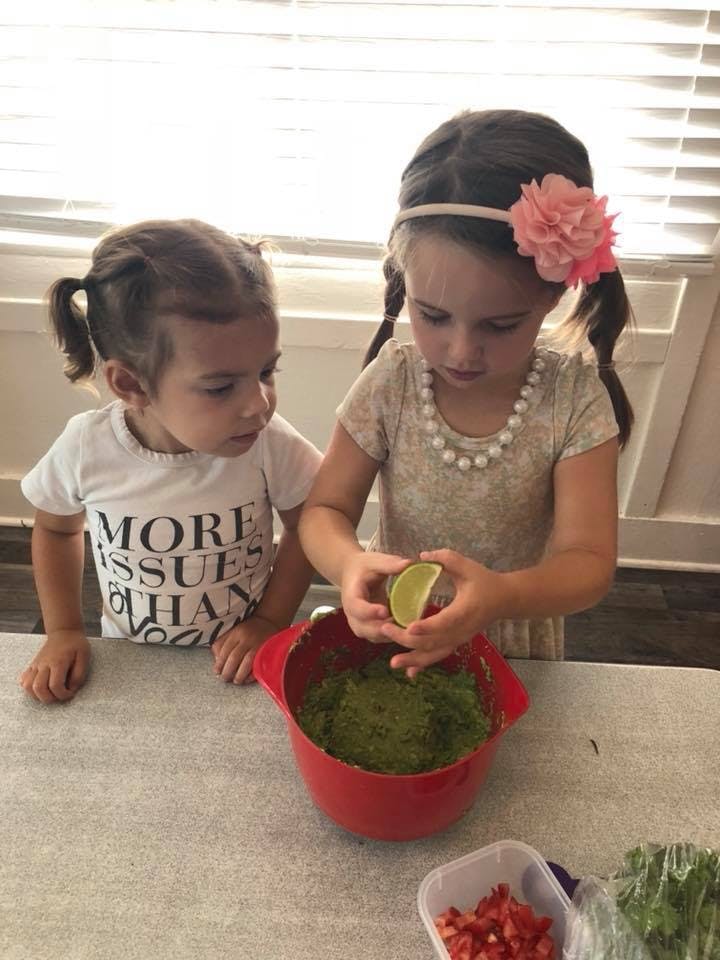 Two children preparing food, one squeezing a lime into a red bowl