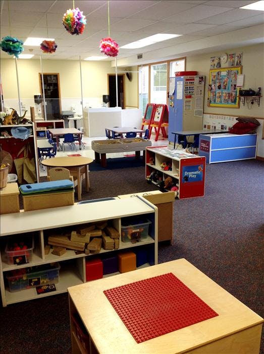 A classroom with small tables, chairs, and play areas