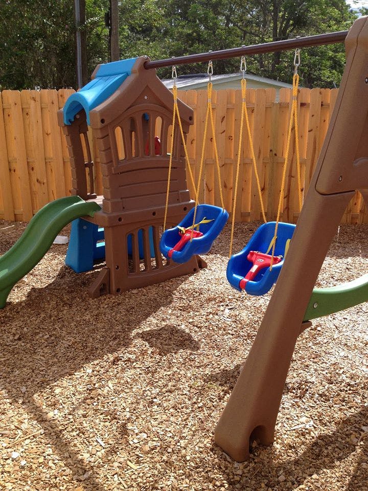 Playground with a slide, two swings, and wood chips on the ground