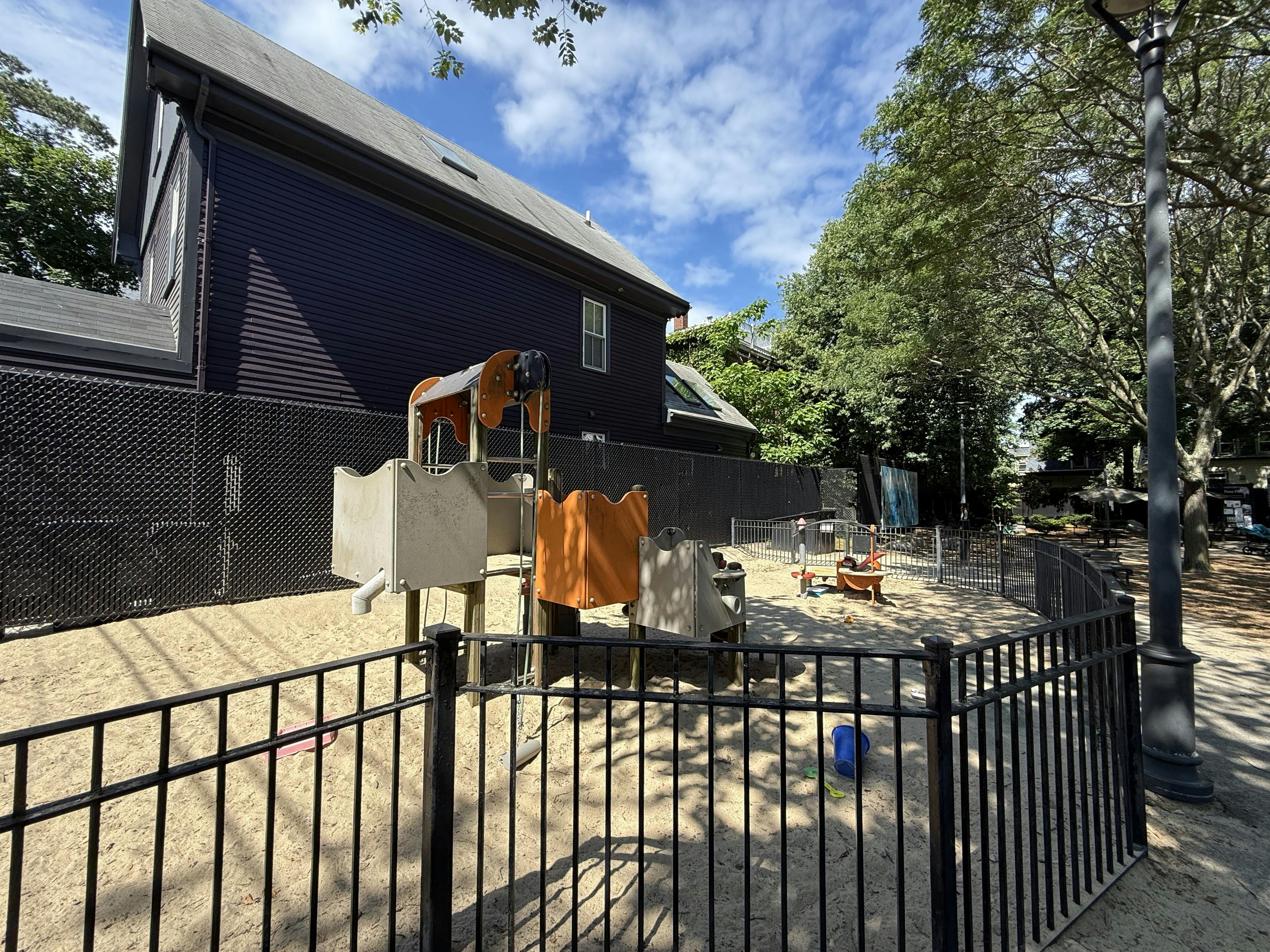 Playground with sand, play structures, and a black fence