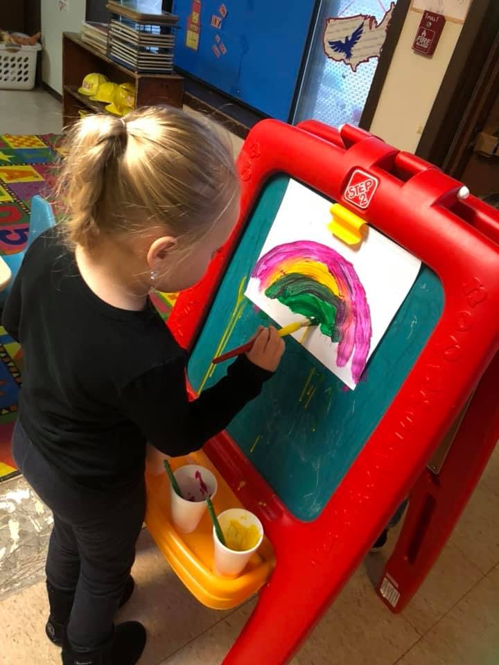 Child painting a rainbow on an easel