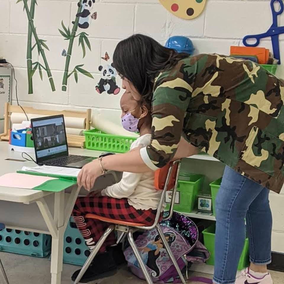 Person helping a child wearing a mask at a laptop