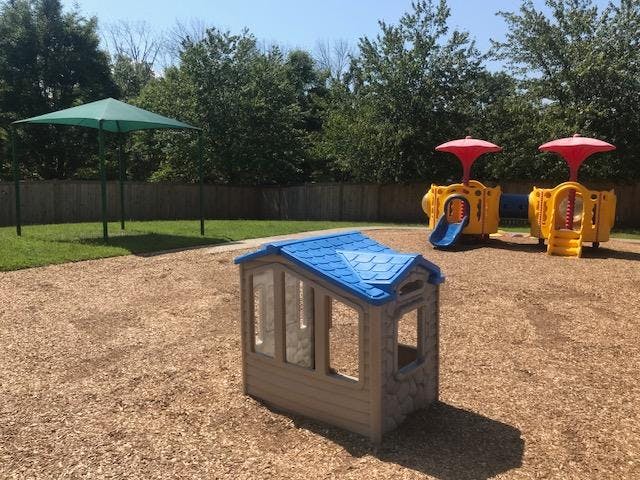 Playground with small house, yellow play structure, and green umbrella shade