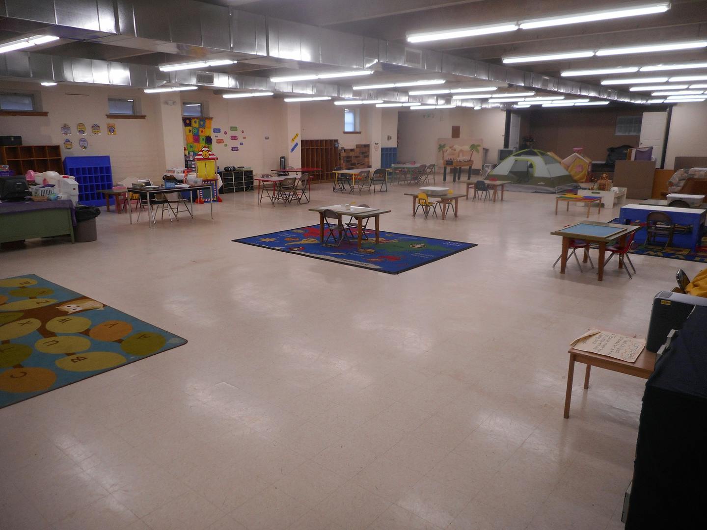 Large empty room with small tables and chairs, two rugs on the floor