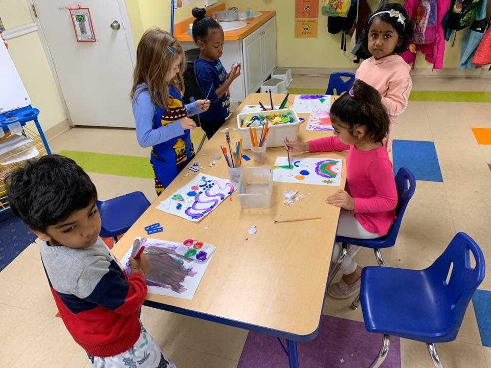 Children drawing and painting at a table in a classroom