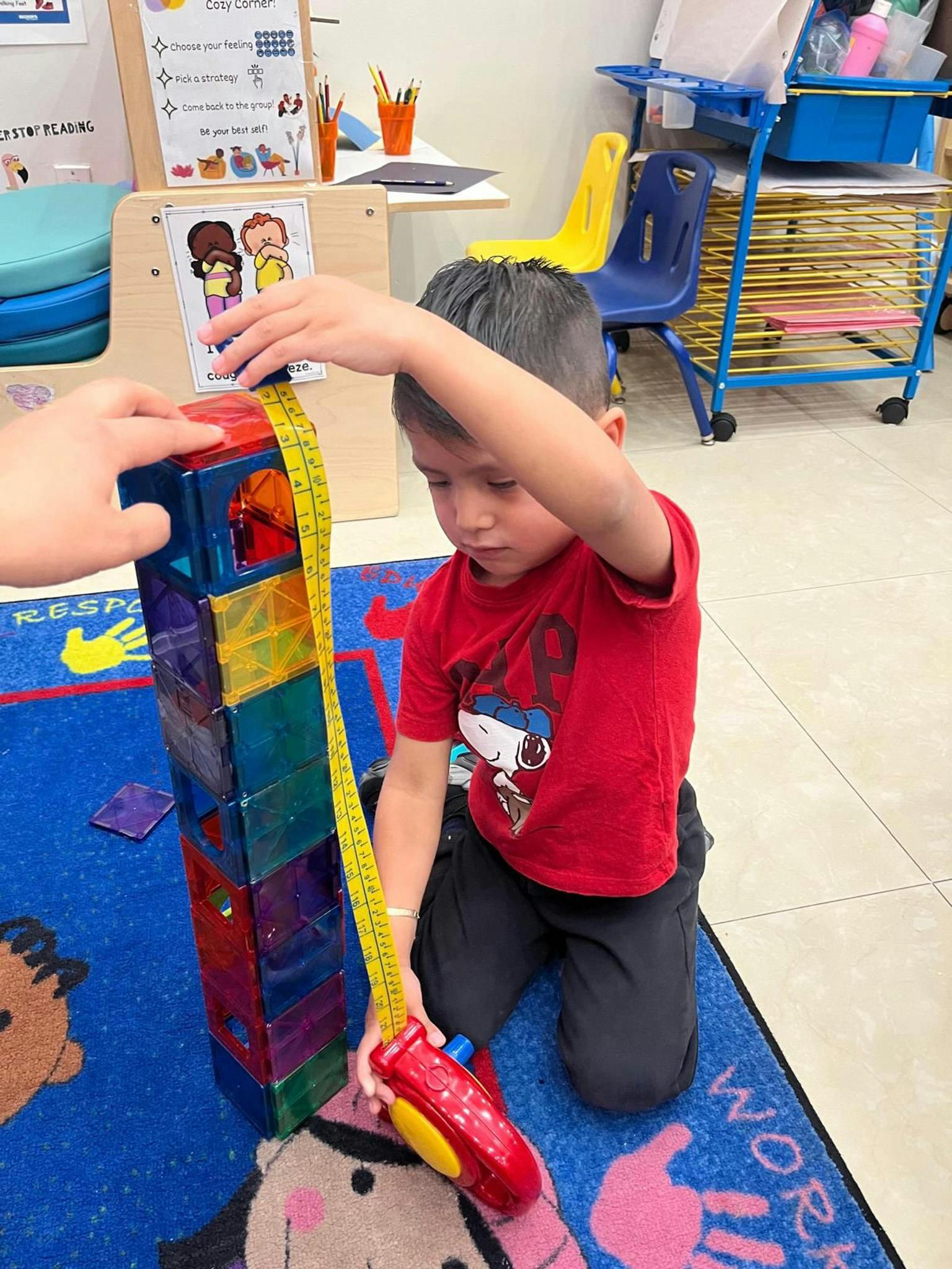 Child measuring a tall stack of colorful magnetic blocks with a tape measure