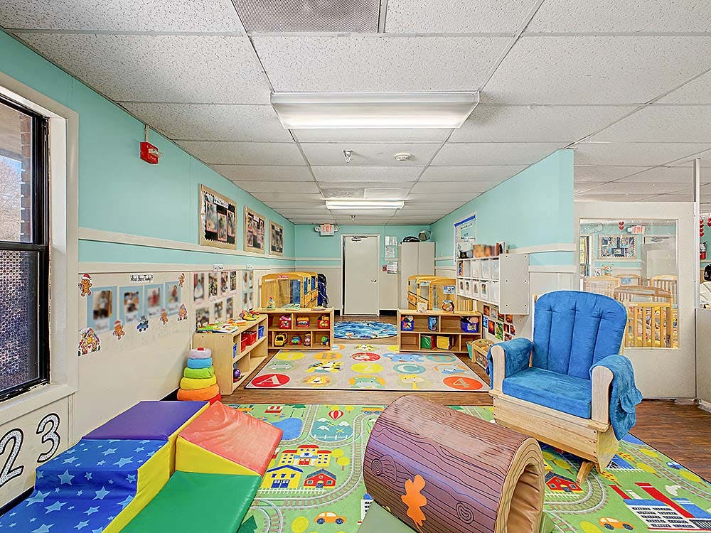 Childcare classroom with colorful rugs, play equipment, and a blue rocking chair