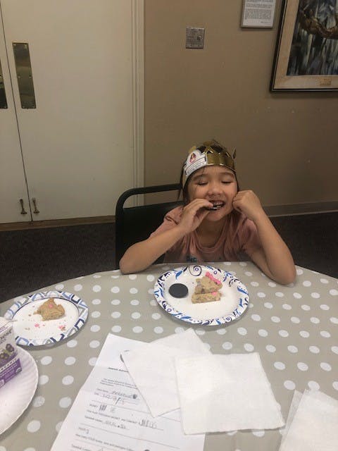 Child wearing a crown eating a cookie at a table