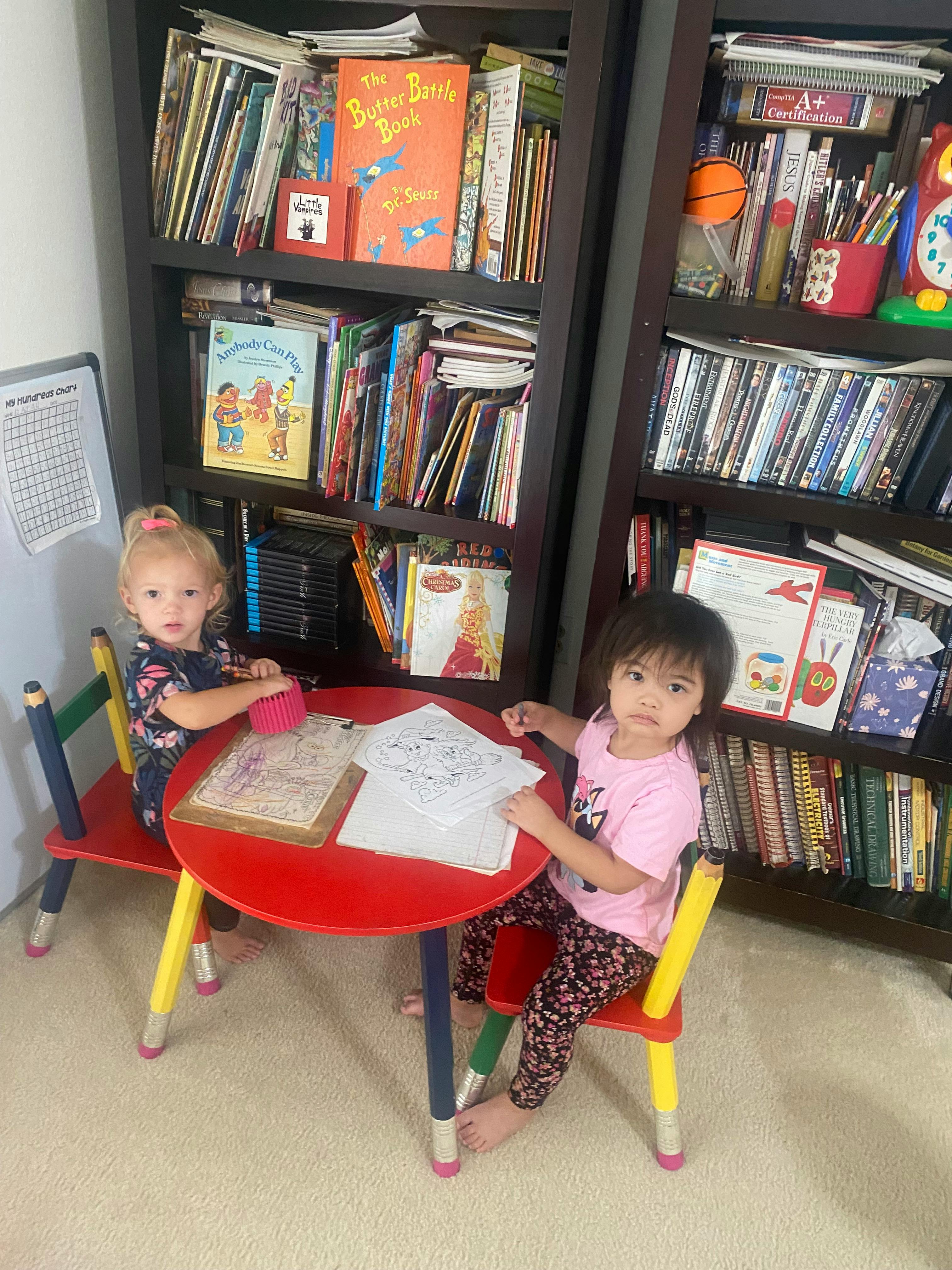 Two children coloring at a small round table in front of a bookshelf