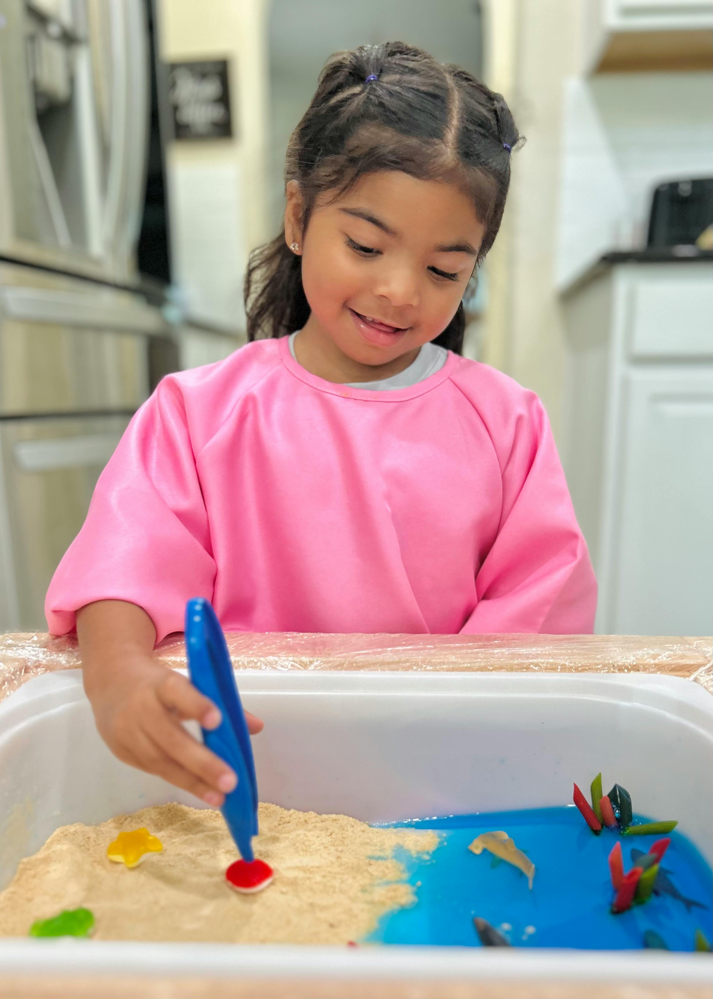 Child in pink smock playing with sand and blue liquid in a bin