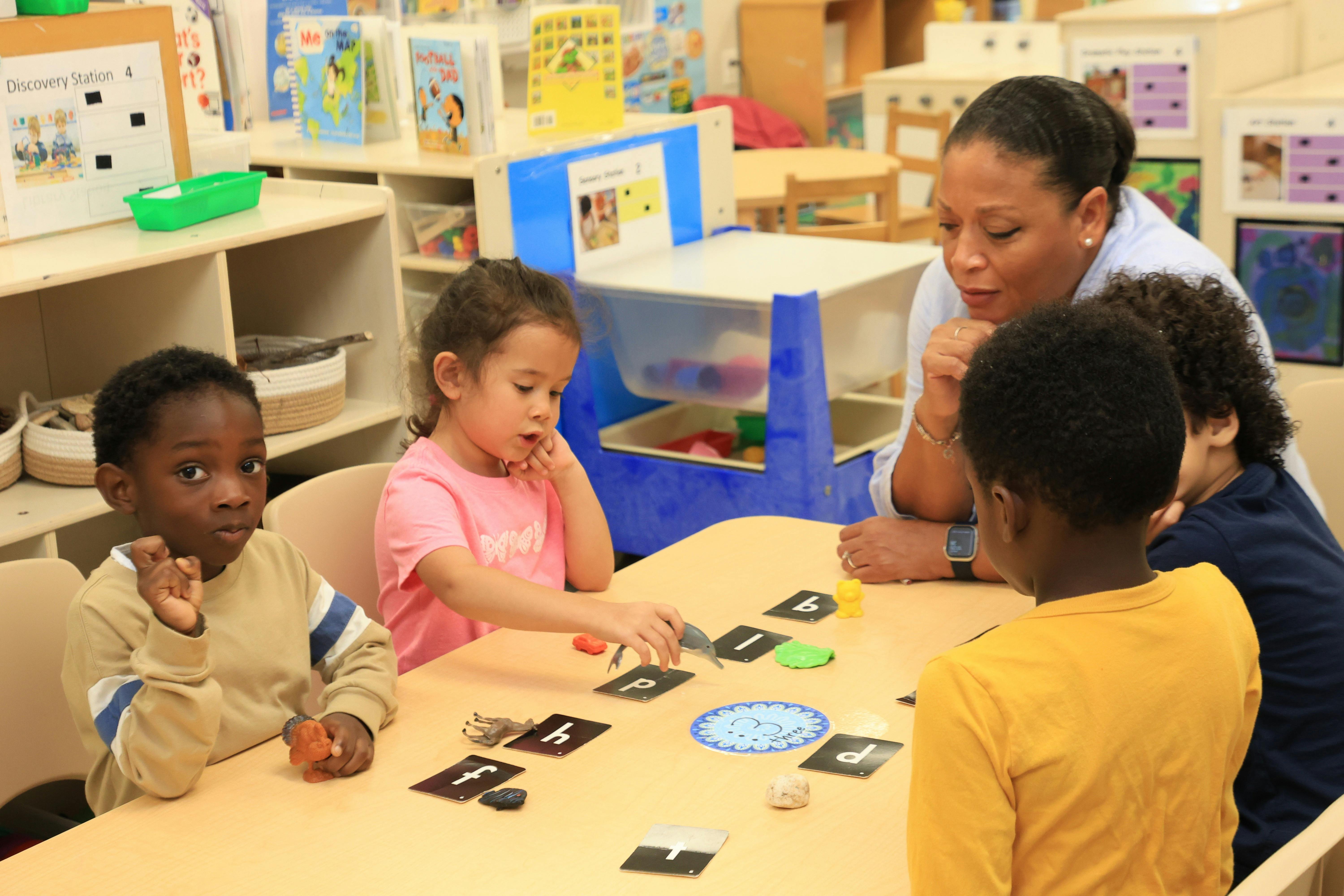Adult and children playing a game at a table in a classroom