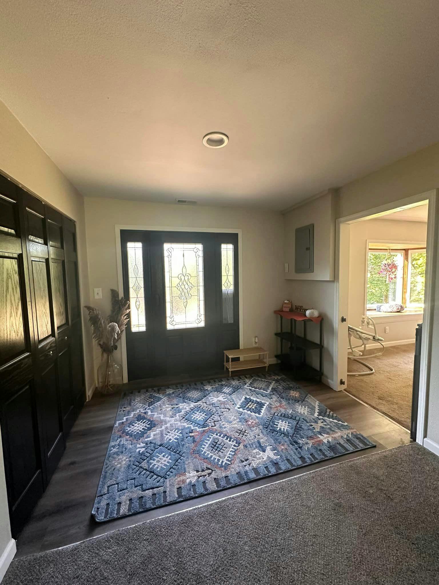 Entryway with a patterned rug, dark front door, and open doorway to another room