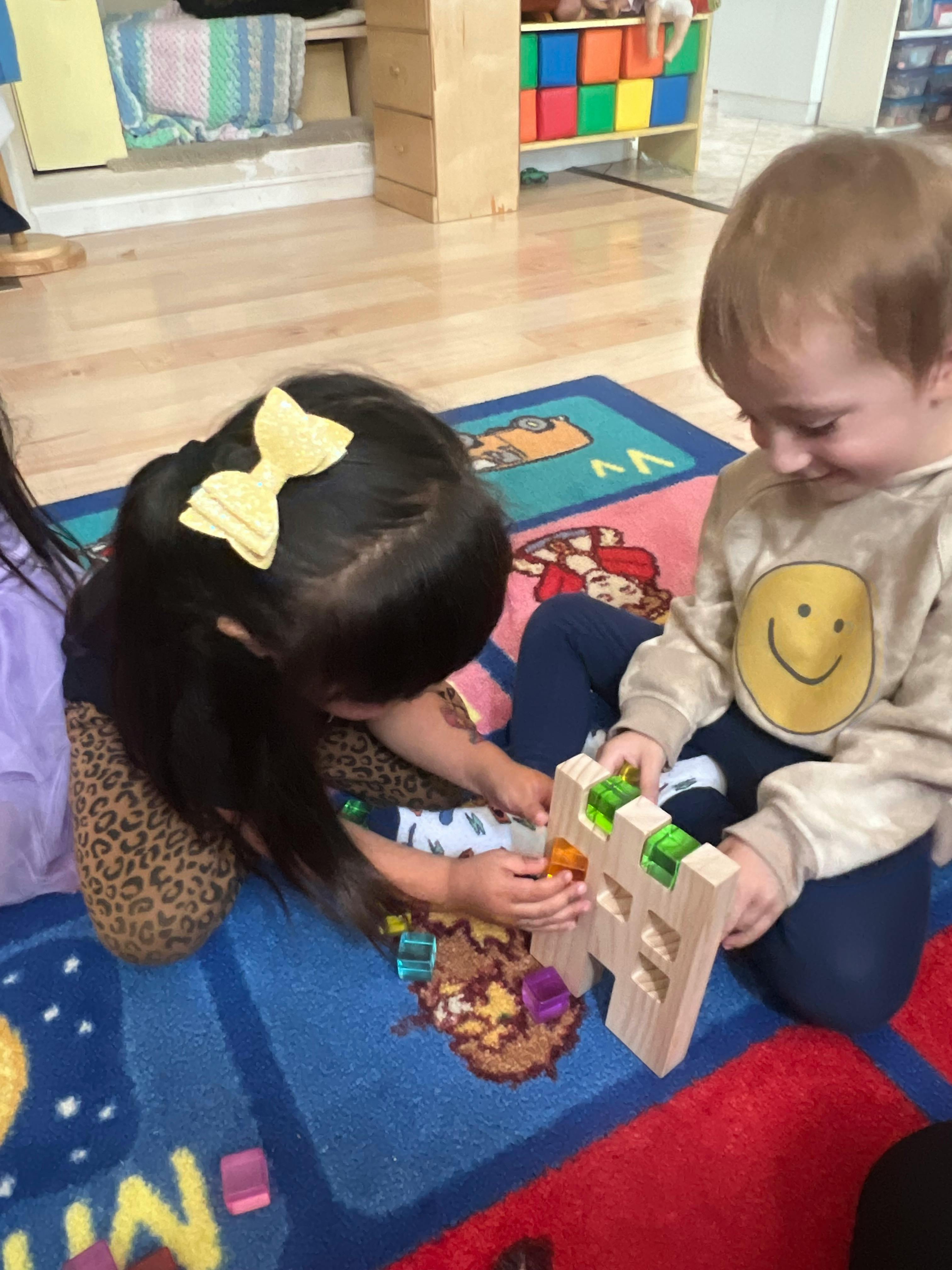 Two children playing with a wooden block toy on a colorful rug